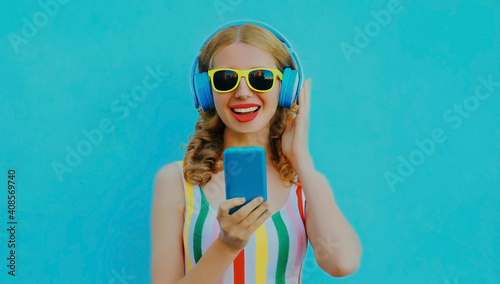 Portrait of happy smiling young woman in wireless headphones with phone listening to music on a blue background