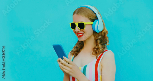 Portrait of happy smiling young woman in wireless headphones with phone listening to music on a blue background © rohappy