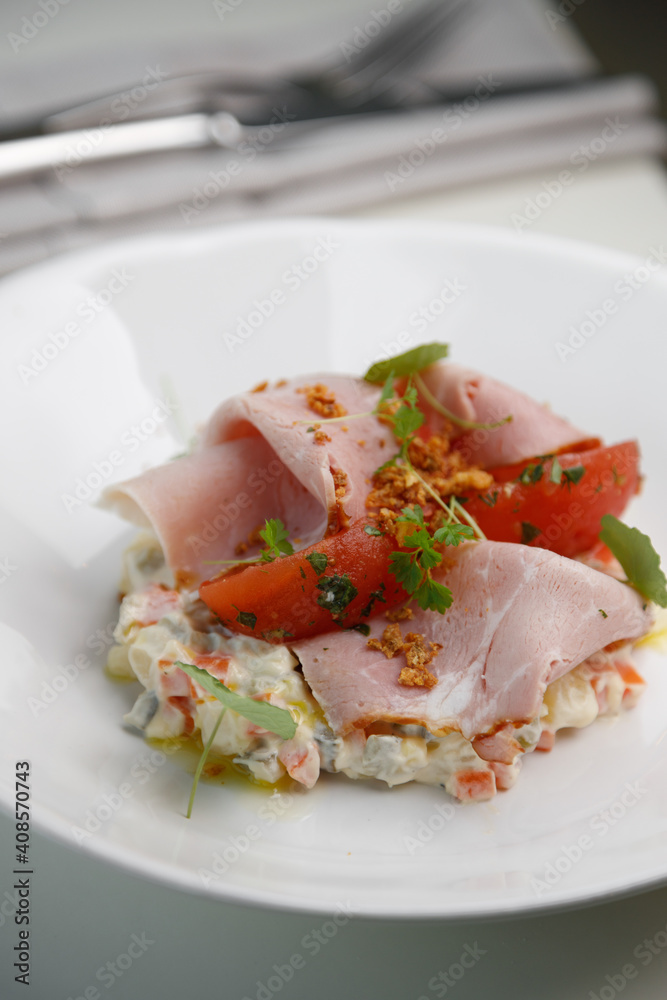 Vegetable salad with ham, parsley and tomato. Restaurant dish on a white plate close-up.