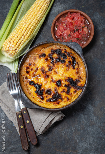 Chilean food. Traditional Pastel de Choclo corn pie. Beef meat with onion, chicken and egg covered with ground corn in clay bowl, top view photo