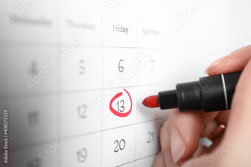 Woman marking Friday 13th on calendar, closeup. Bad luck superstition photo