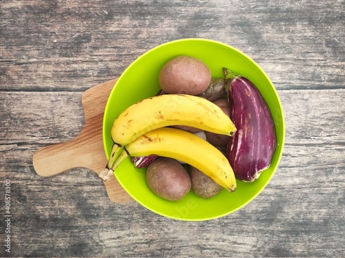 A green bowl with bananas, potatoes and eggplant