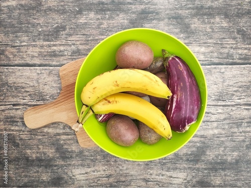 A green bowl with bananas, potatoes and eggplant