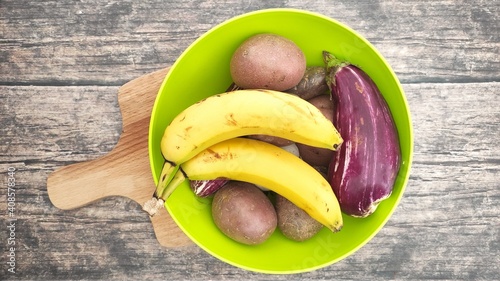 A green bowl with bananas, potatoes and eggplant