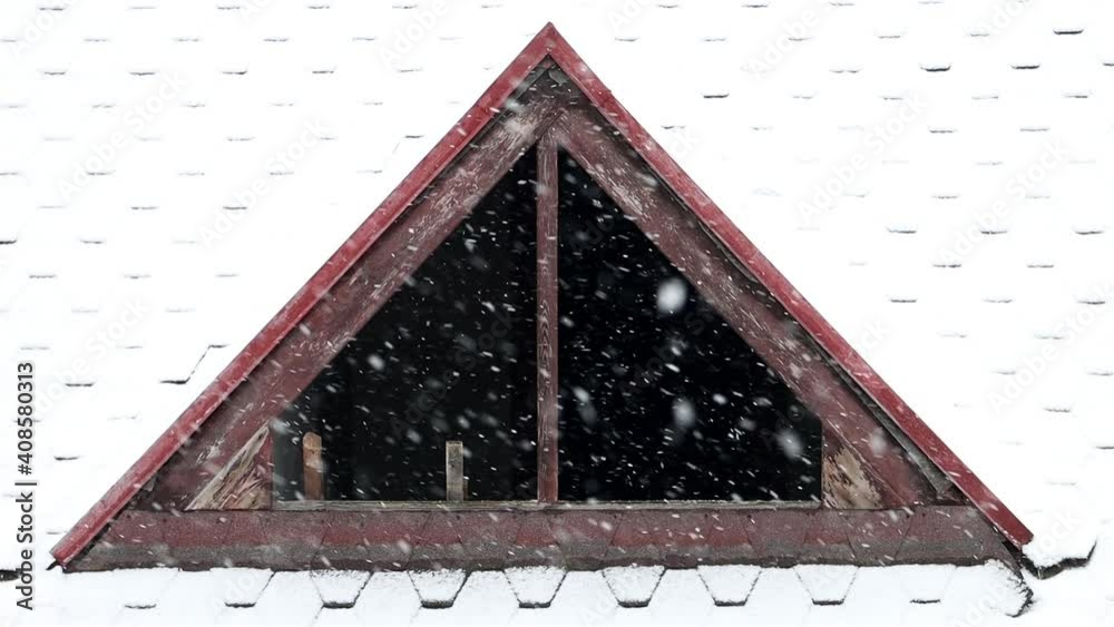 The dormer without glass in the windows on the snowy roof. Falling snow on the roof of the house with a window without glass.