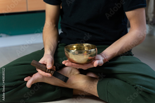 A man plays singing bowl sitting at the floor. Mind and body relationship. Traditional sound healing ceremony. 