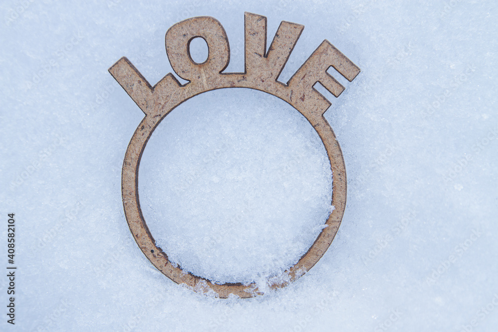Word love and ring cut out of plywood lie on snow background with copy space. Word love and ring cut out of plywood lie on snow background with copy space.