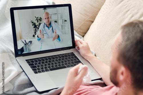 Young sick man with laptop and crumpled handkerchief consulting online doctor