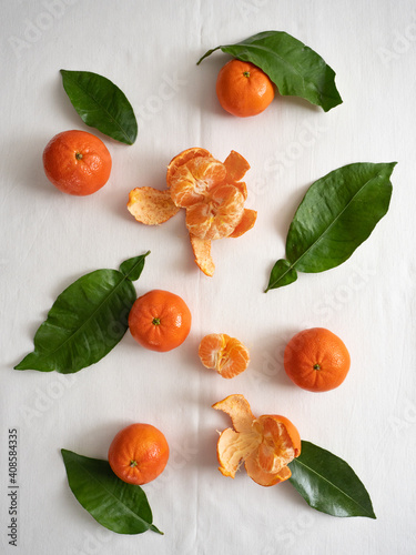 Fototapeta Naklejka Na Ścianę i Meble -  Fresh juicy bright orange tangerines with green leaves on a white cotton tablecloth in the morning light