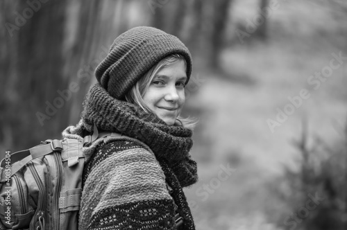 Black and white portrait of a young woman with layers of heavy winter clothes, wool scarf and hat looking at camera and smiling during a country hike.