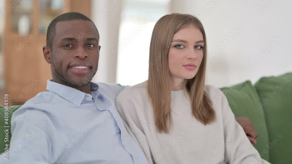 Mixed Race Couple Sitting on Sofa and Smiling at Camera Mixed Race Couple Sitting on Sofa and Smiling at Camera