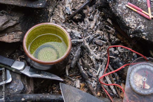 Wallpaper Mural Close up shot from above of a small green china tea cup with water in and a camping knife at the side on the now cold ashes of what was a small campfire. Torontodigital.ca