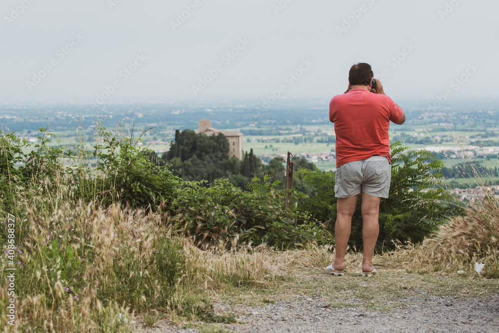 20 September 2020, Italy. A tourist in shorts and slippers stops on the road to photograph a castle