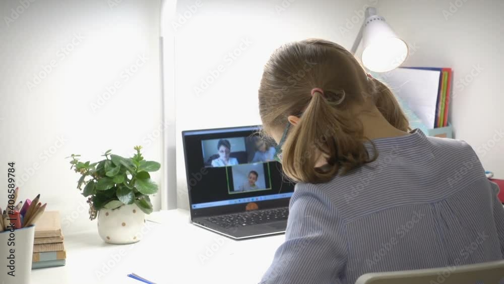 Cute school girl at online lesson with her teacher using laptop during digital homeschooling
