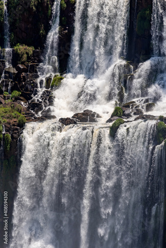 Powerful splashing water stream of famous Iguazu Falls flowing from rocky formation covered with green plants