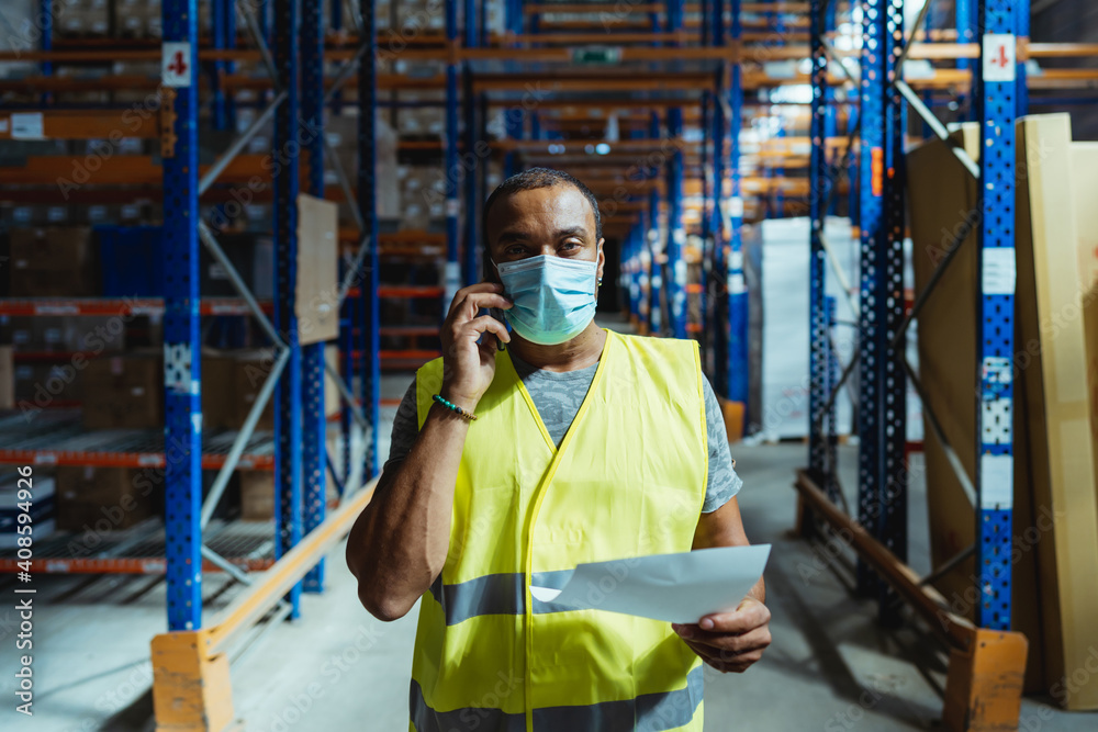 40 years old warehouse manager talking on the phone and wearing a protective mask