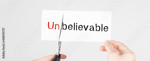 Scissors cutting white paper with the text unbelivable, change word to belivable. photo