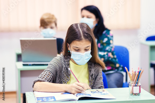 Children and teacher with face mask back to school in classroom after covid-19 lockdown photo