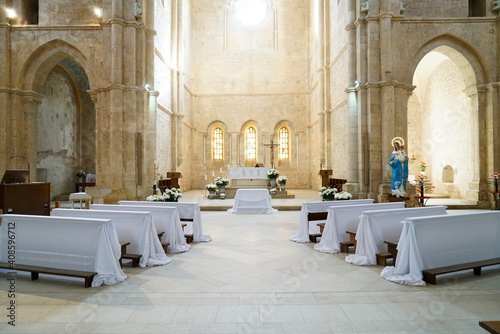 interno di una abbazia medievale con banchi coperti da teli bianchi pronti per la celebrazione delle comunioni dei bambini , effetto di luce del rosone in alto photo