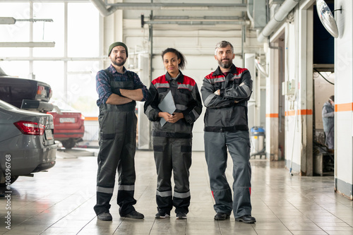Young cheerful intercultural workers of car repair center standing in workshop