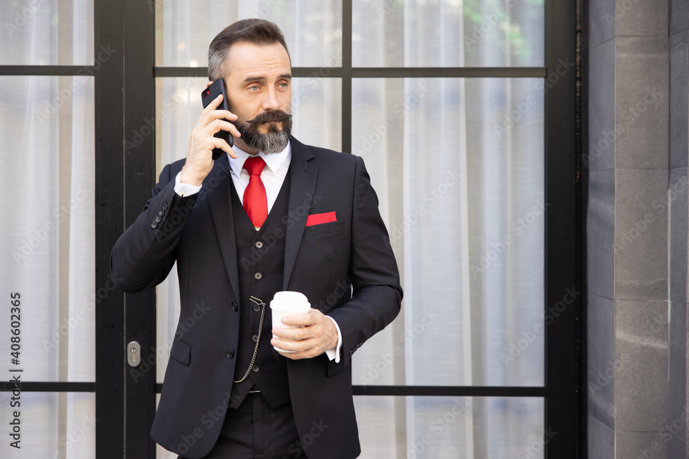 Businessman in Suit Holding a Cup of Coffee While Talking on His Mobile Phone Businessman in Suit Holding a Cup of Coffee While Talking on His Mobile Phone