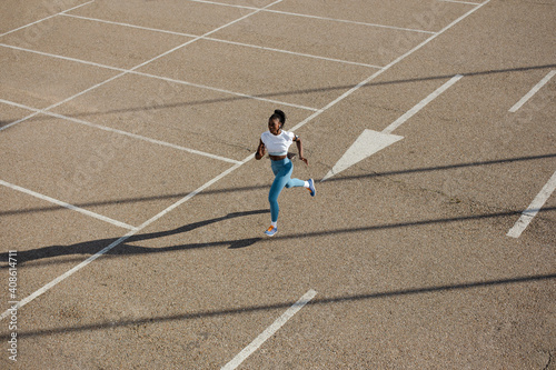 Powerful female athlete running on urban asphalt. Sporty young black woman training in the city.