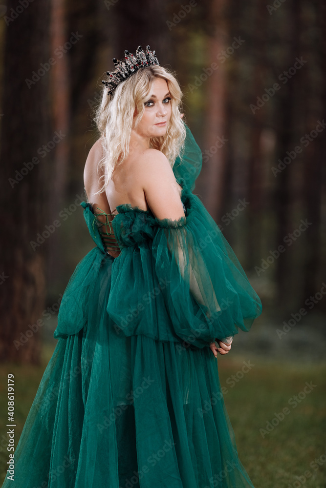 young beautiful blonde hair woman queen. Princess walks. autumn green forest mystic. Vintage medieval shiny crown. Long evening green dress. magic fantasy. back view young beautiful blonde hair woman queen. Princess walks. autumn green forest mystic. Vintage medieval shiny crown. Long evening green dress. magic fantasy. back view
