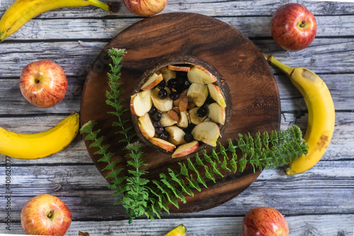 tabla redonda de madera con un bol de coco rellena de ensalada de frutas con manzanas y plátanos alrededor 