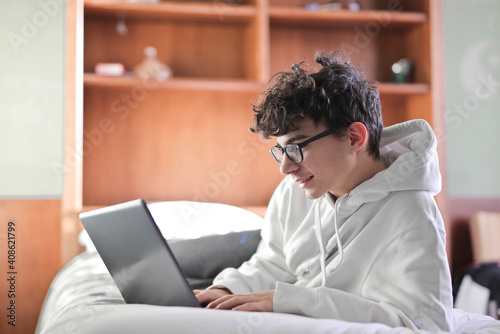 portrait of young boy lying on the bed with a computer