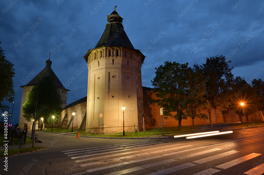 Obraz premium Night view of a monastery with high red towers and walls, with dramatic dark blue clouds in the sky. 