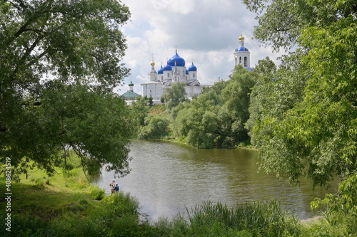 Old orthodox monastery with gold and blue domes surrounded by green summer trees and a lake, located in Bogolyubovo, Russian 
