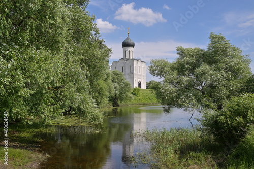 Famous Russian Pokrova-na-Nerli medieval orthodox church, reflecting in a lake, surrounded by green summer trees. 