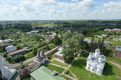 Bird-view panorama from a bell tower of old Russian town of Suzdal with orthodox churches, wooden houses and green fields up to the horizon. 