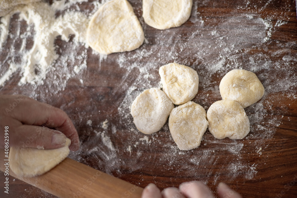 Fototapeta premium Senior woman hands rolling out dough in flour with rolling pin in her home kitchen