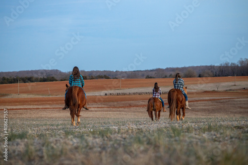Young Women Riding Horses Through Farm Field