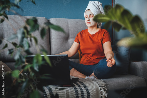 Girl with face mask and bath towel sitting on sofa and meditating in yoga pose yoga at home, quarantine, lockdown, meditation, mental health, wellness,self-care photo