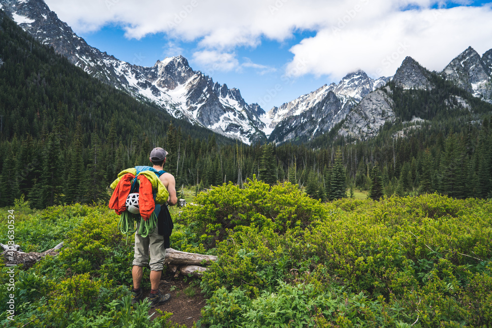 Man standing with backpack in field against mountain backdrop Man standing with backpack in field against mountain backdrop