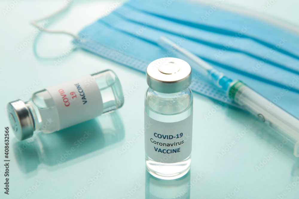 Coronavirus or COVID-19, 2019 - nCoV vaccine in a bottle with syringe and hygiene protective face mask on eflective surface. Coronavirus or COVID-19, 2019 - nCoV vaccine in a bottle with syringe and hygiene protective face mask on eflective surface.