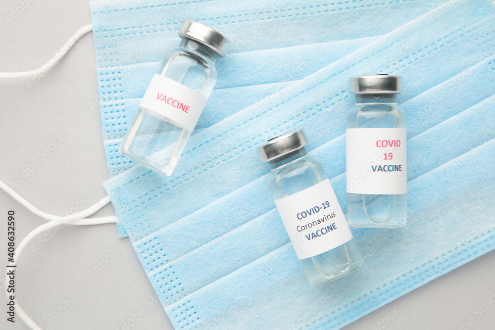 Coronavirus or COVID-19, 2019 - nCoV vaccine in a bottle with hygiene protective face mask on eflective surface.