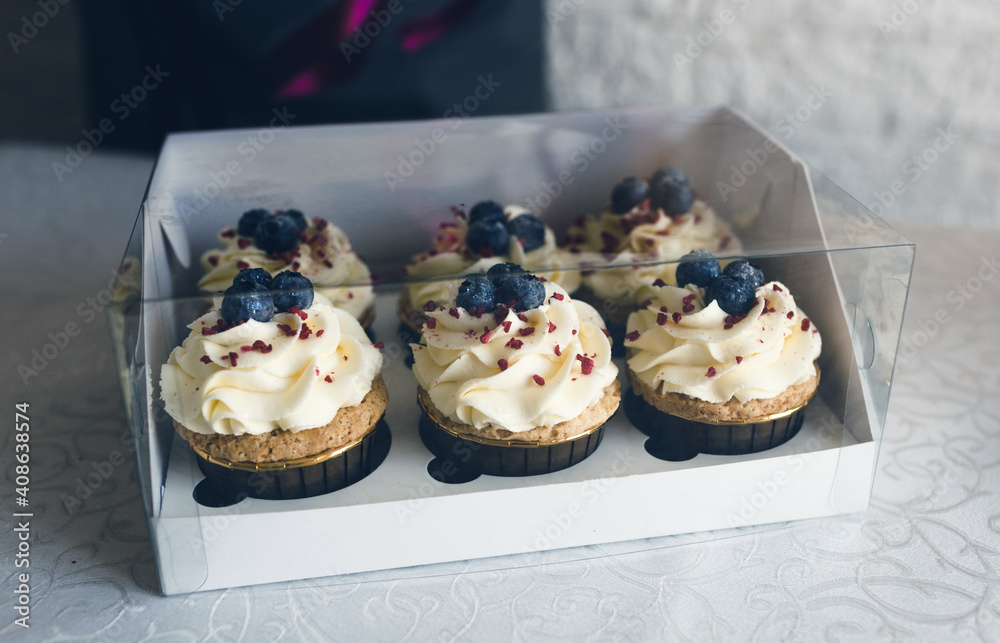 A girl cook in a gray apron packs cupcakes with cream in a gift box to send the order to the customer. A girl cook in a gray apron packs cupcakes with cream in a gift box to send the order to the customer.