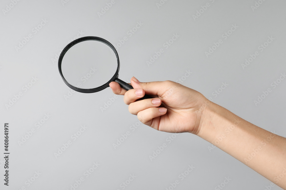 Woman holding magnifying glass on grey background, closeup. Find keywords concept Woman holding magnifying glass on grey background, closeup. Find keywords concept