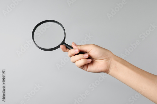 Woman holding magnifying glass on grey background, closeup. Find keywords concept