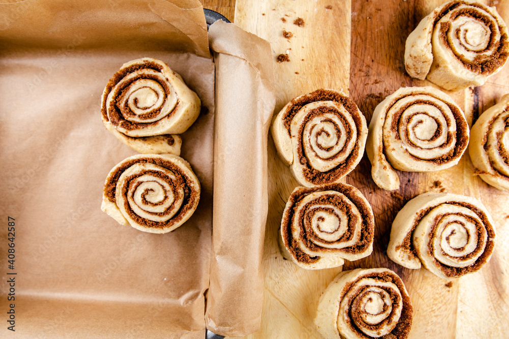 Cinnamon rolls laid on a table being put into a baking tray Cinnamon rolls laid on a table being put into a baking tray