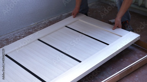a man lays a light wooden canvas in a frame, bleached larch in the renovation of the room design, installing a door into a box during the installer's work