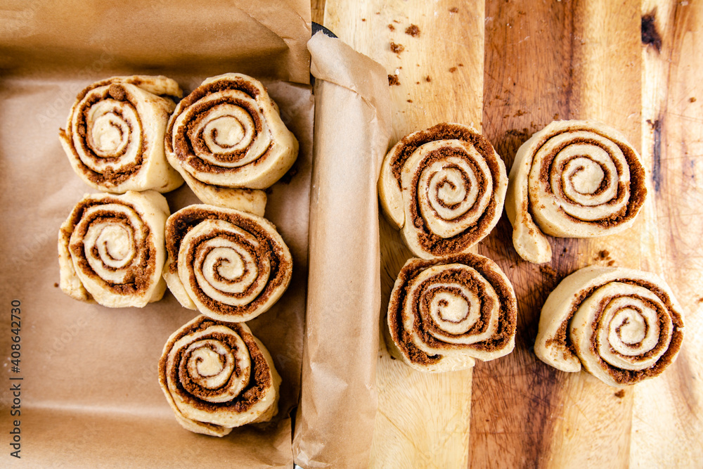 Cinnamon rolls laid on a table being put into a baking tray Cinnamon rolls laid on a table being put into a baking tray