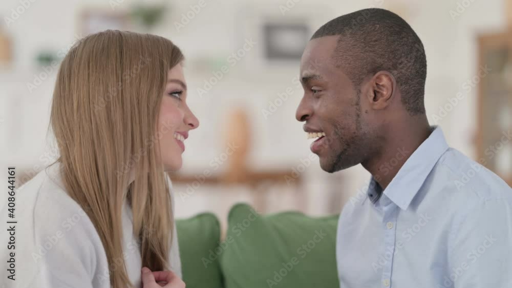 Loving Mixed Race Couple having Conversation while Sitting on Sofa Loving Mixed Race Couple having Conversation while Sitting on Sofa