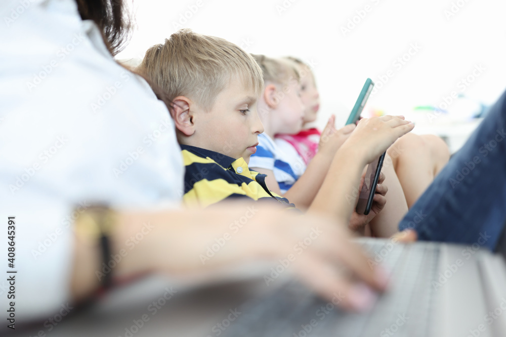 Children sit on couch and play on their smartphones. Addiction of modern children to gadgets concept Children sit on couch and play on their smartphones. Addiction of modern children to gadgets concept