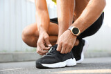 Man with fitness tracker tying shoelaces outdoors, closeup