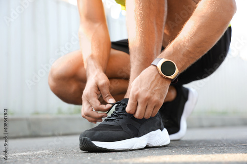 Man with fitness tracker tying shoelaces outdoors, closeup