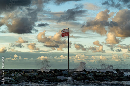 The Polish flag hung on a mast by the sea.